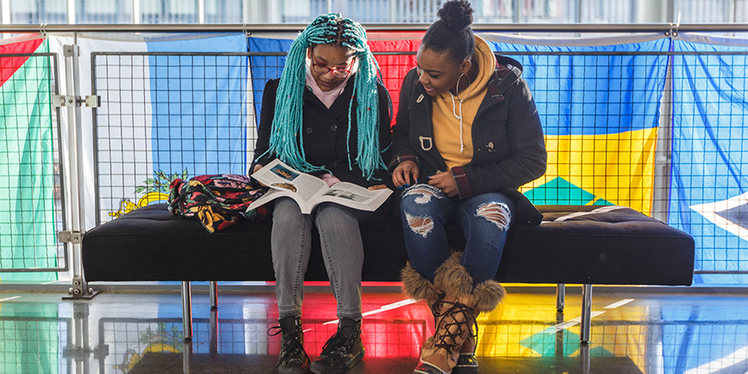 Two students sit in the campus center look at a book.