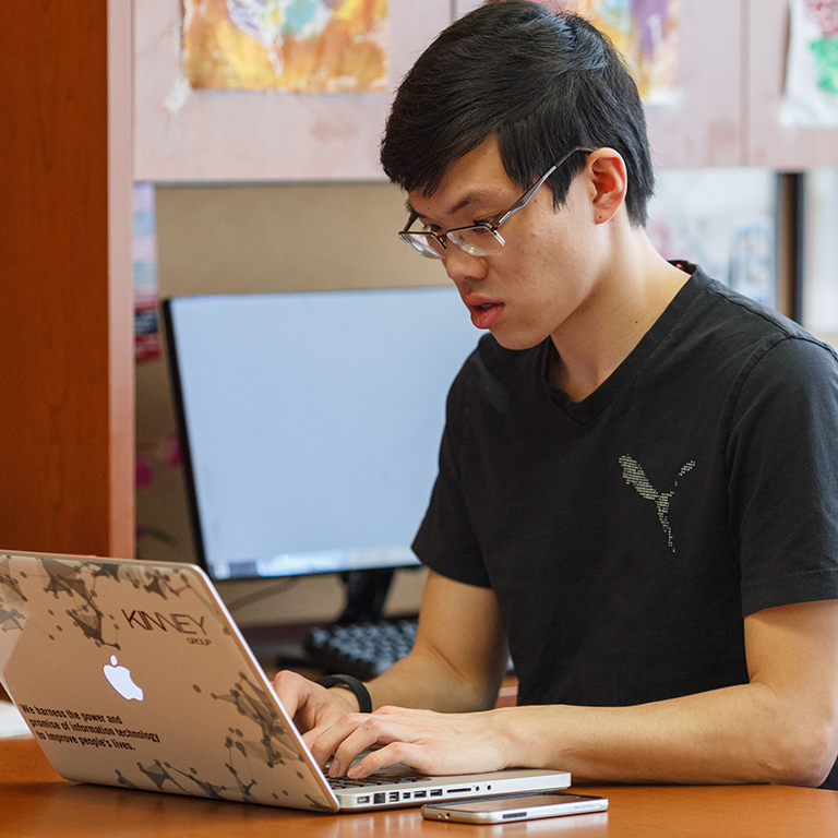 Student typing on a MacBook laptop.