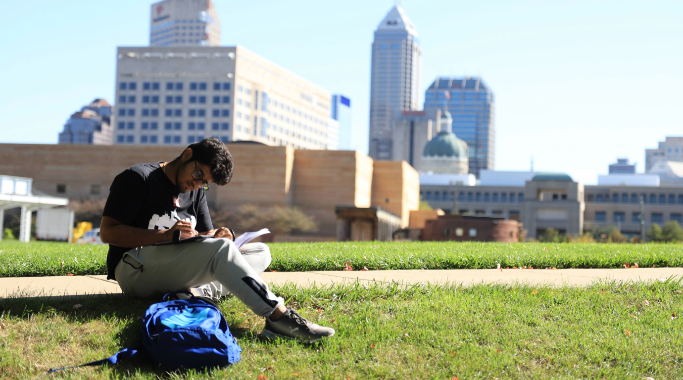 Student studying by White River State Park with the Indianapolis skyline in the background